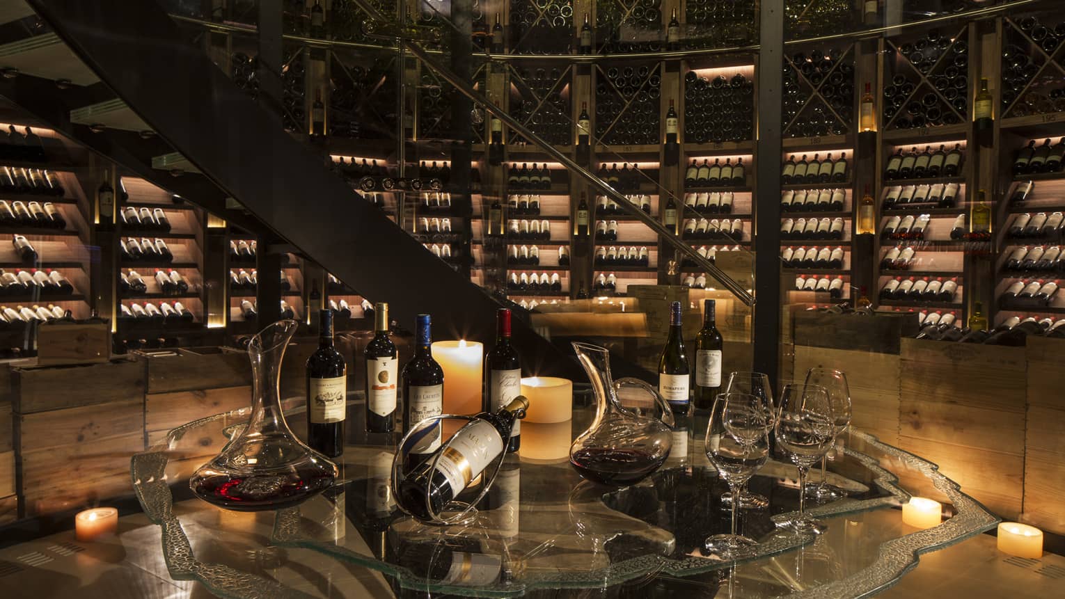 Bottles of wine are arranged for a tasting within an expansive, candlelit wine cellar