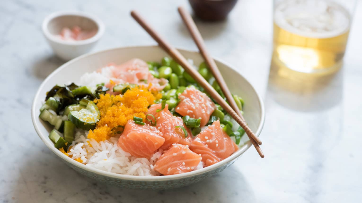 Chopsticks on poke fish bowl with chunks of raw salmon, edamame beans, cucumber, roe on rice 