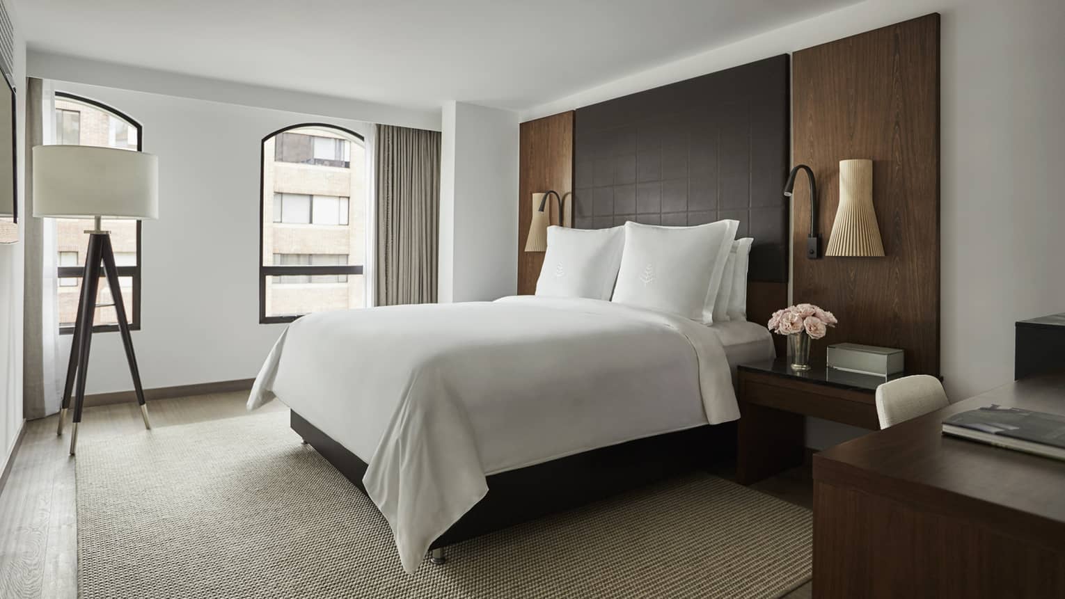 Deluxe Room bed with crisp white linens, leather and wood headboard, wood tripod lamp with white shade