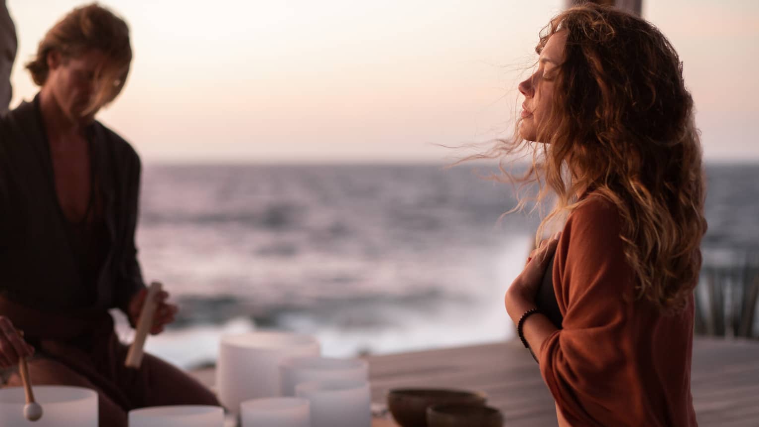 A woman participating in breathwork and sound meditation outside near an ocean.