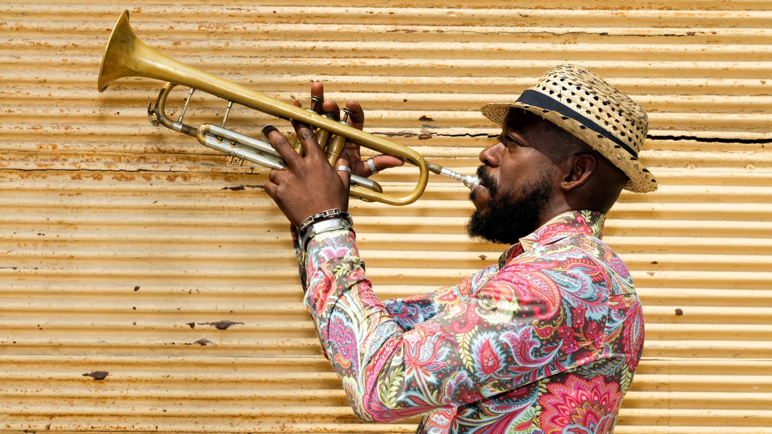 A man in a hat and colourful shirt playing a trumpet.