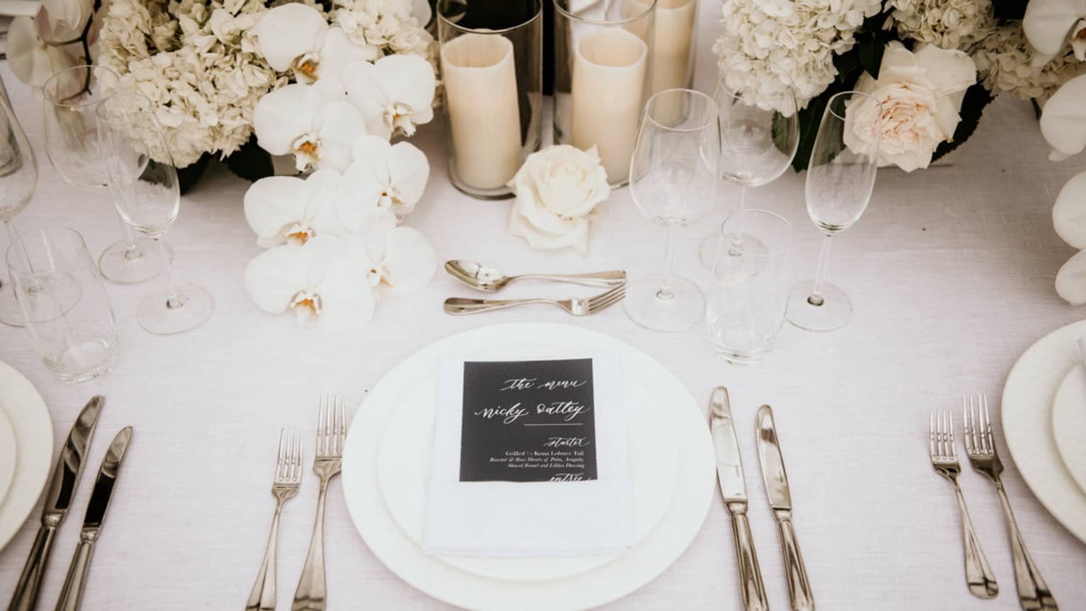 Wedding table setting with white flowers and candles, menu on white napkin and plates