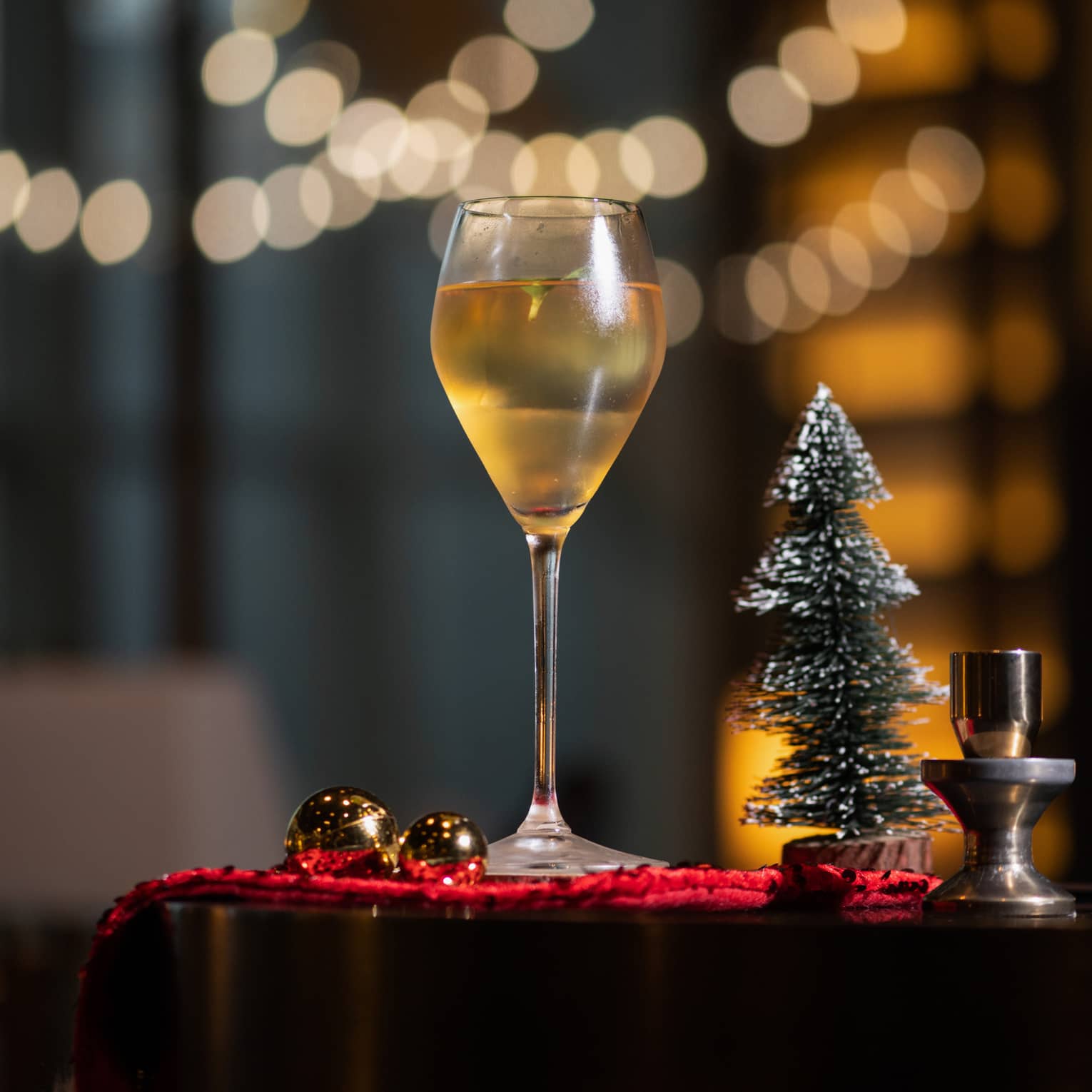 A glass of wine next to a tiny Christmas tree.