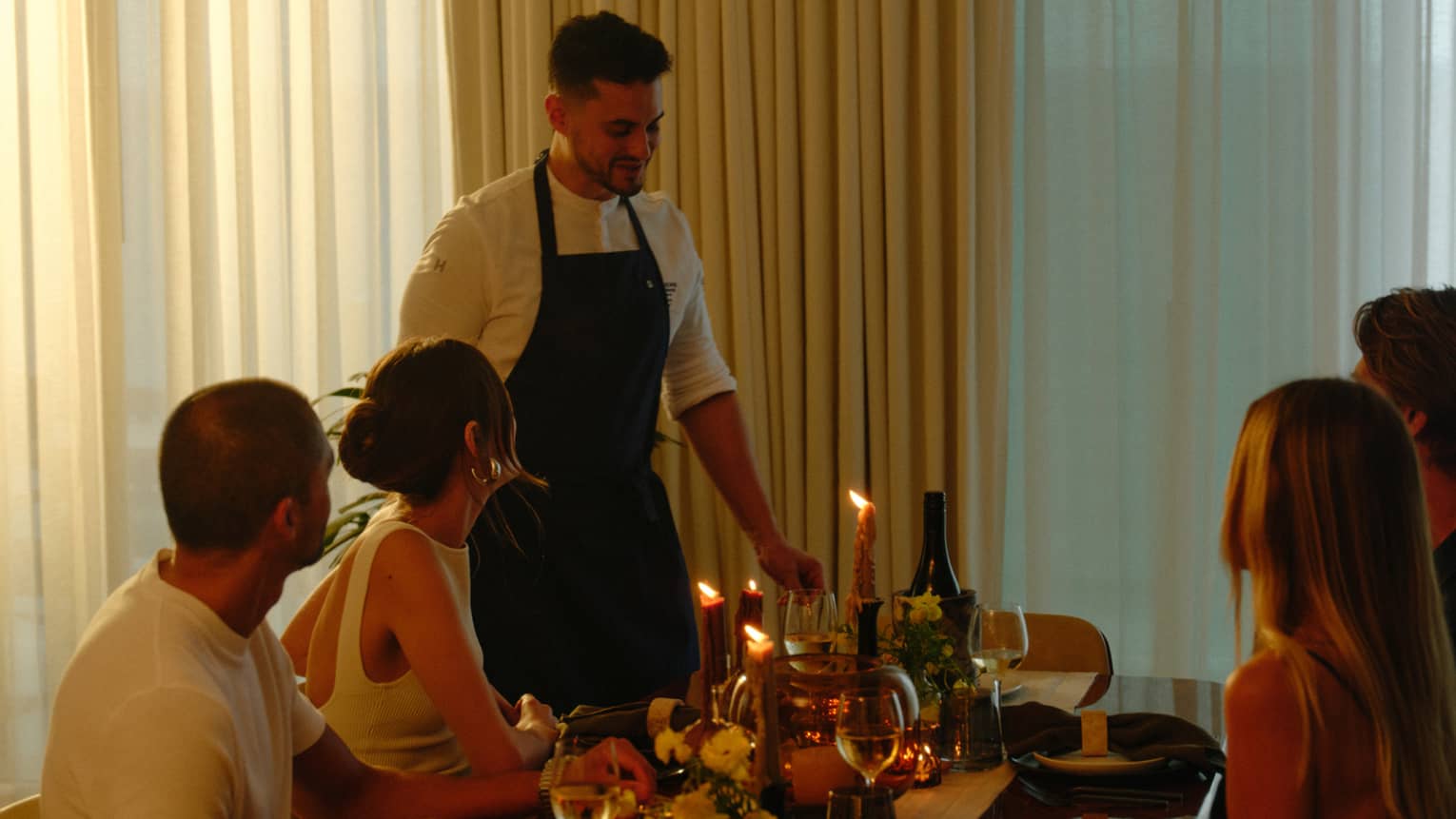 Group of four sits for a meal in a private residence while a chef brings the plates
