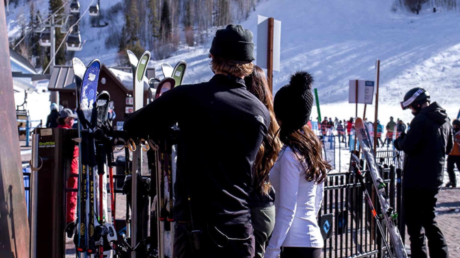 A group of people looking at skis and snowboards outside near a hill with snow on it.