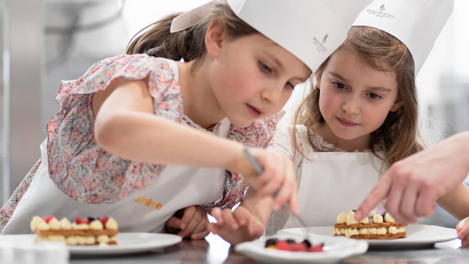 Two children in chef hats carefully decorating plates of desserts during a pastry-making class