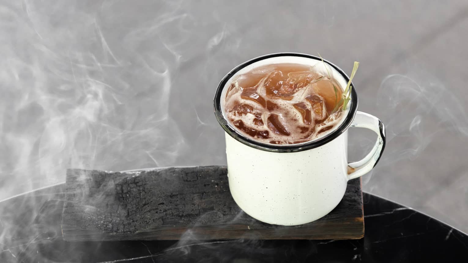 A brown cocktail with ice in a white mug.