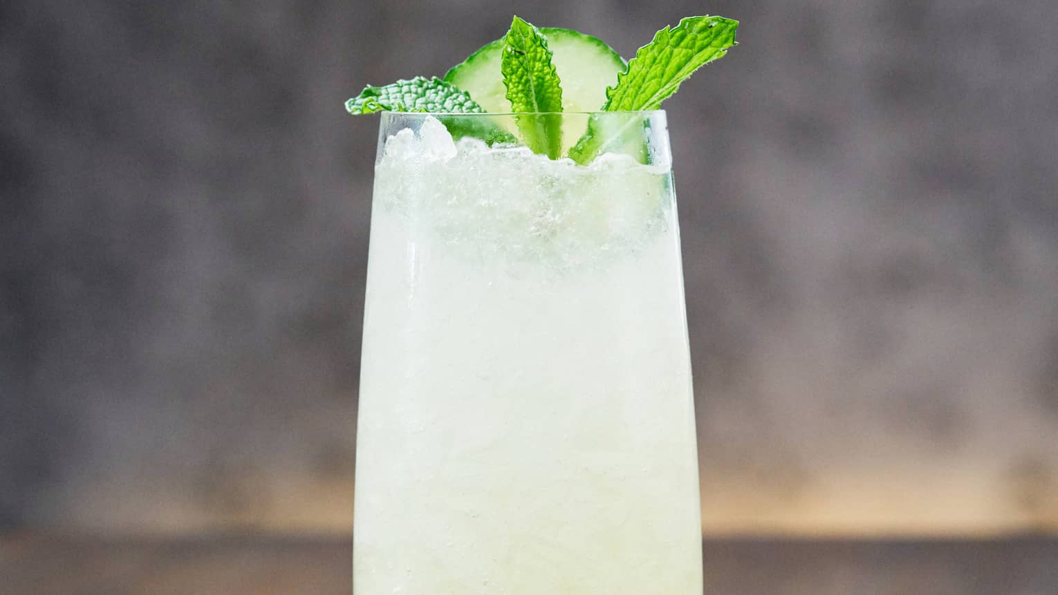 A tall cocktail that is light green in colour with a mint leaf and lime on top.