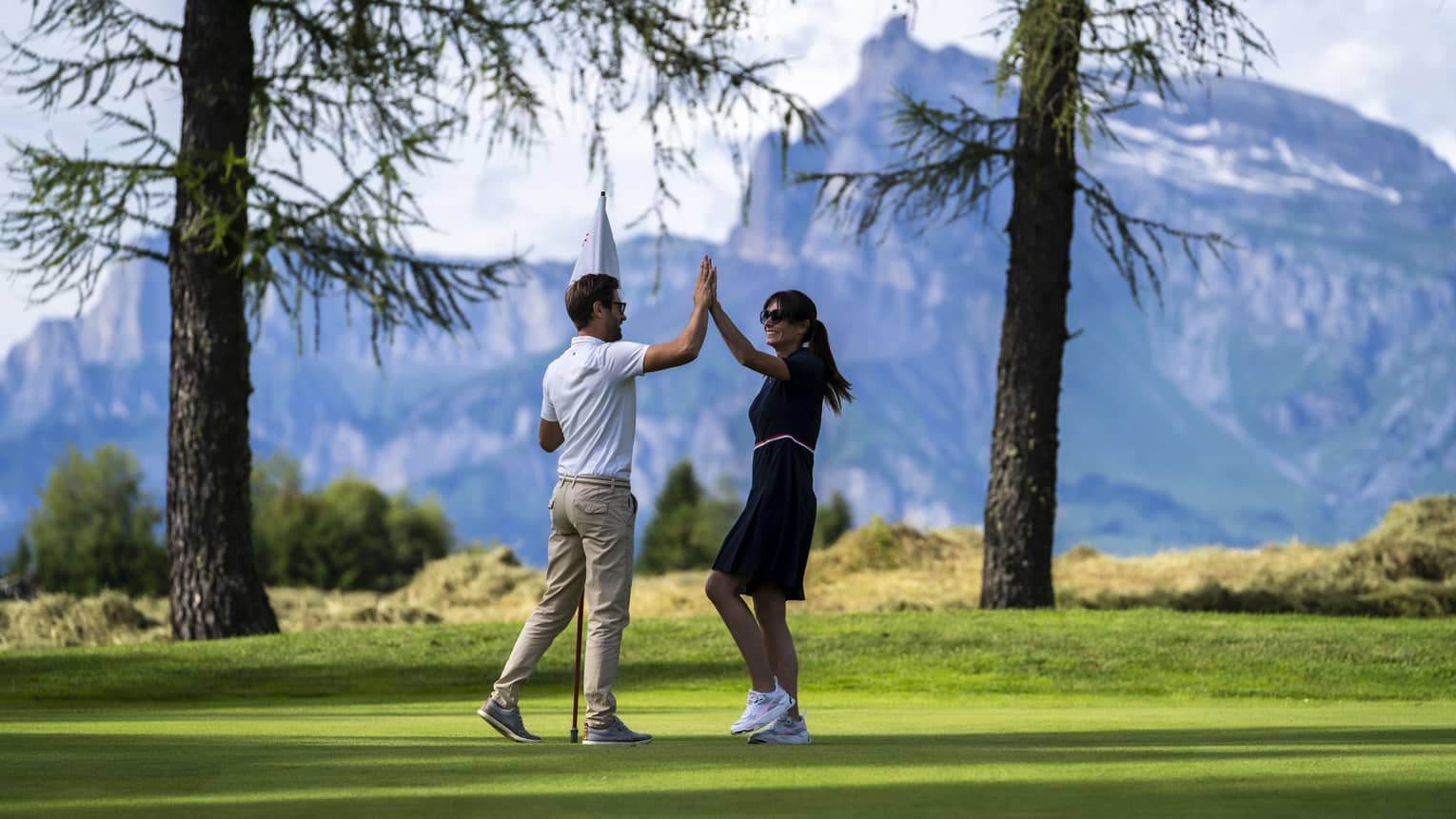 Two people high-fiving on a golf course with mountains in the distance