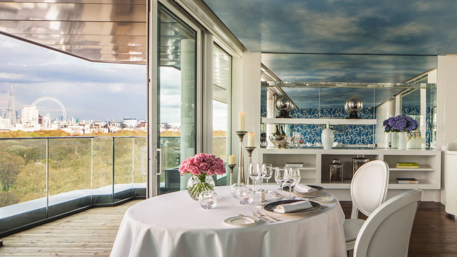 Amaranto restaurant, round dining table with white linens pink roses by open wall, glass balcony