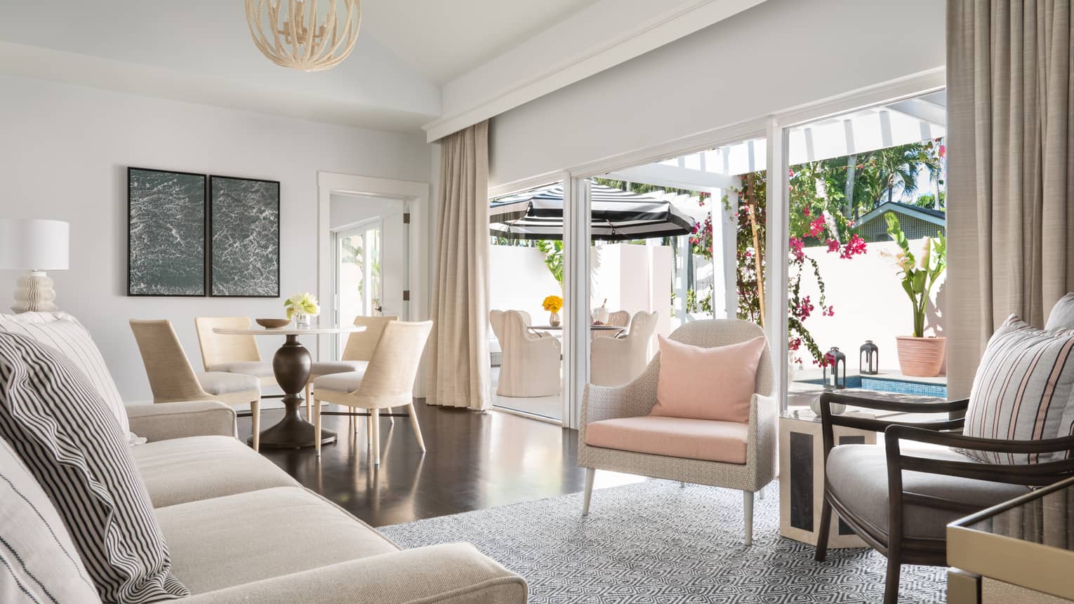 Plunge pool living room with neutral tones, featuring a sofa, dining table and sliding doors opening to an outdoor patio with seating and vibrant flowers