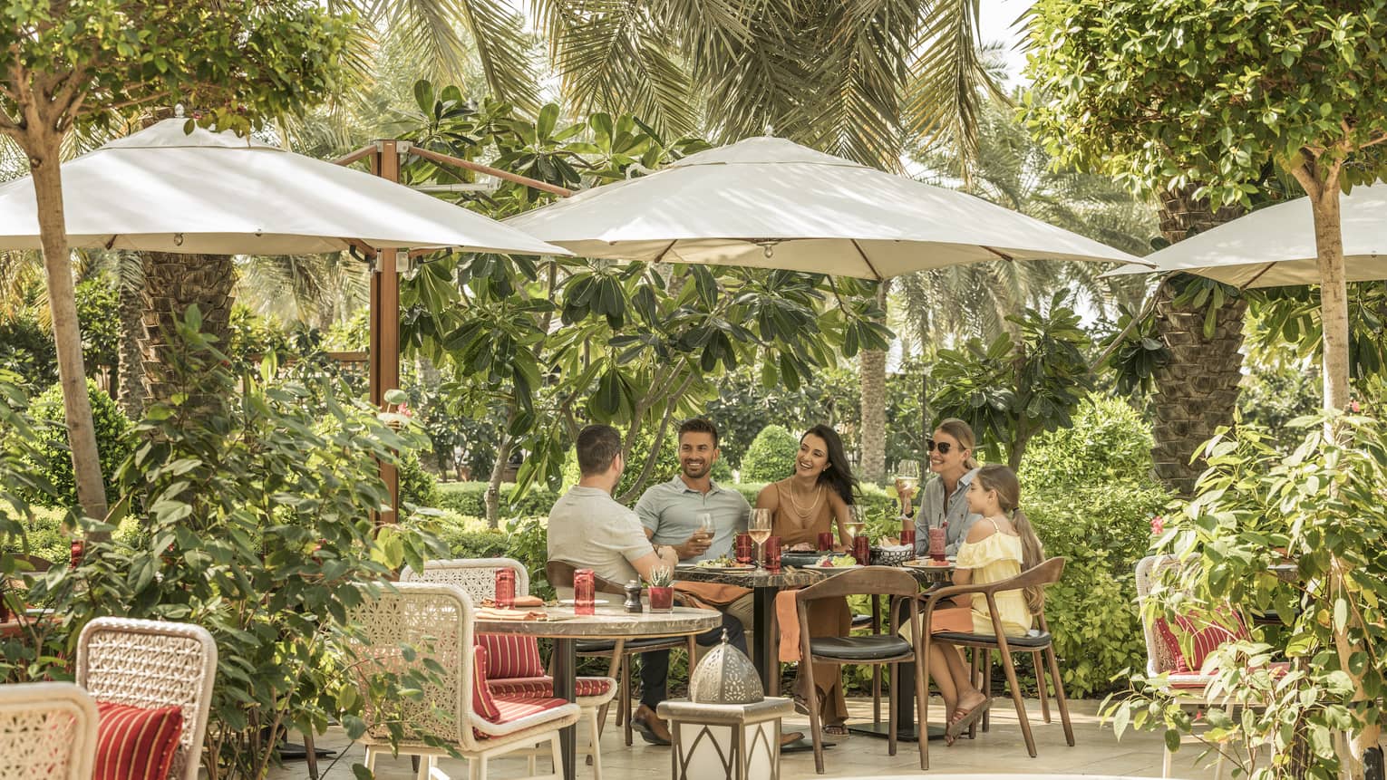 Two couples and a child dine outdoor under an umbrella on SUK's patio surrounded by trees and vegetation