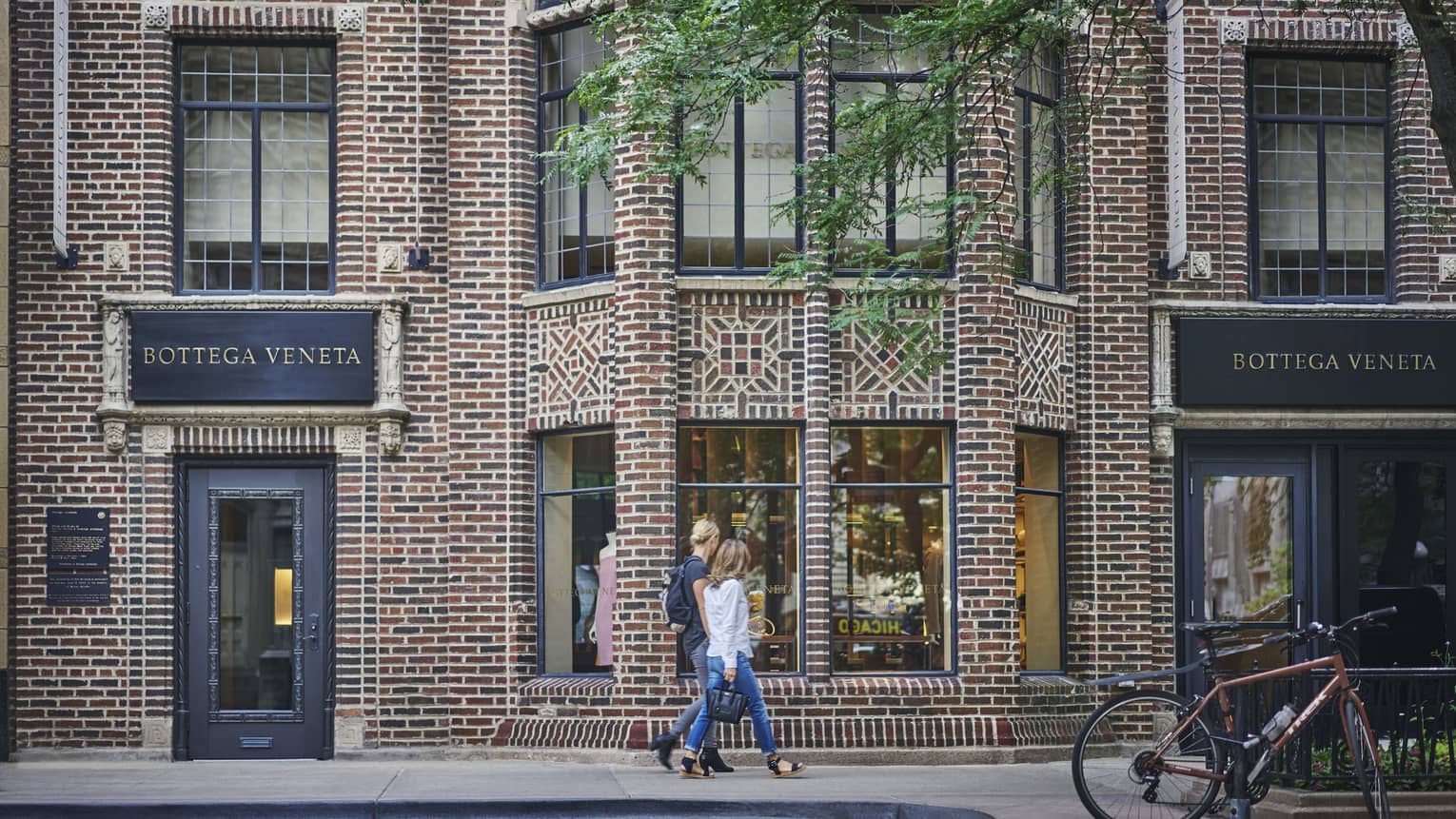 Two people walking down a street with brick buildings.