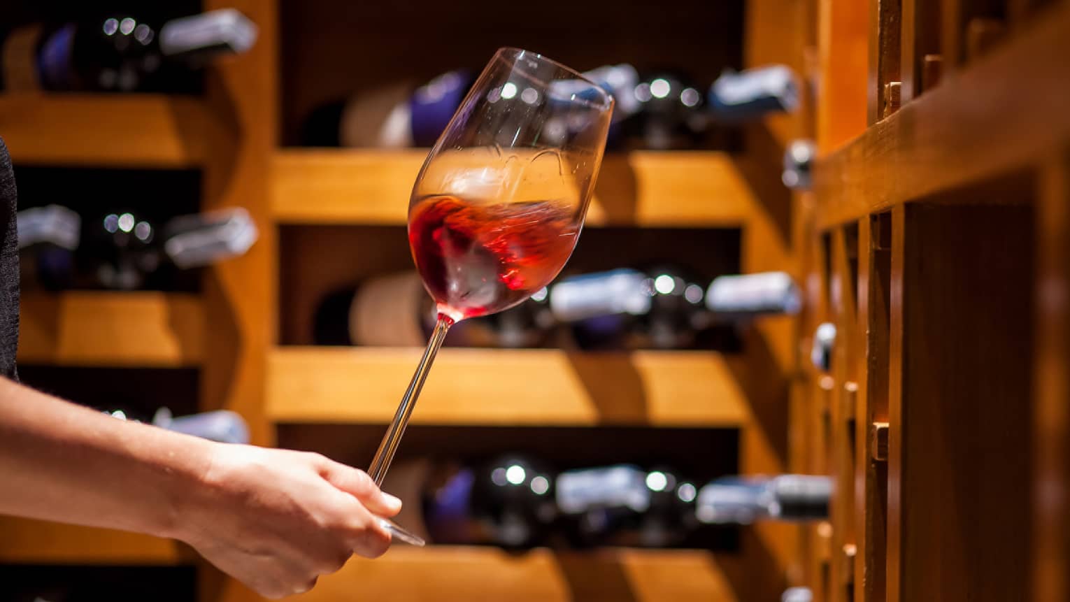 A hand holding a glass of red wine in a wine cellar