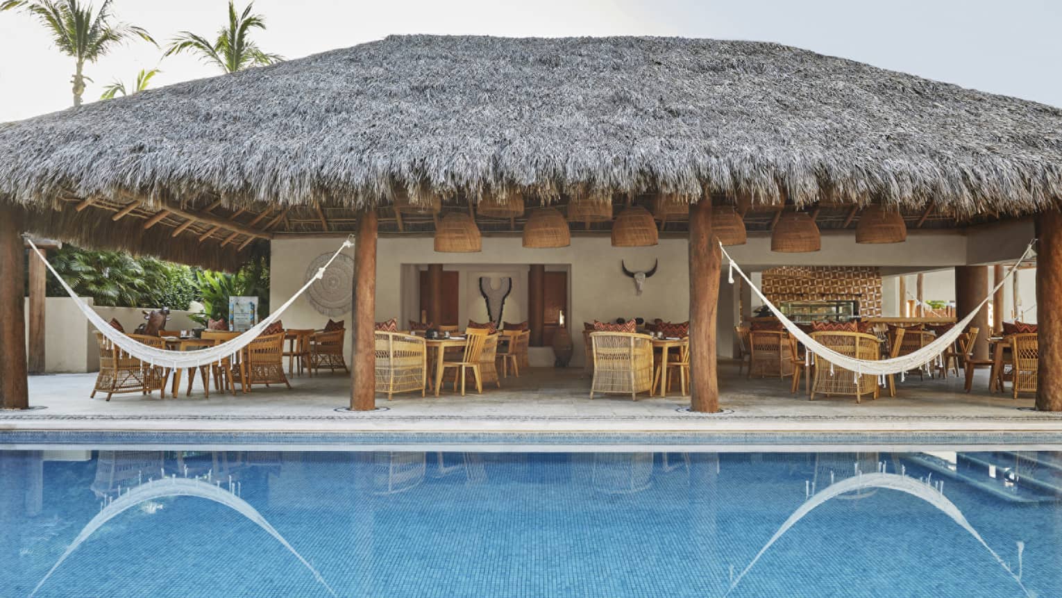 Outdoor lounge set under thatched-roof pavilion next to pool