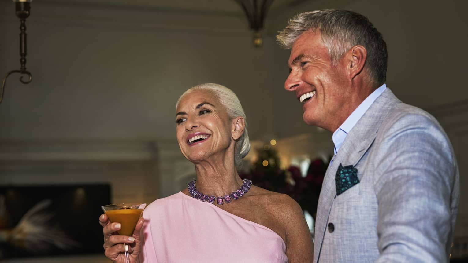 Man in suit and woman in pink dress holding wine glasses at the bar.