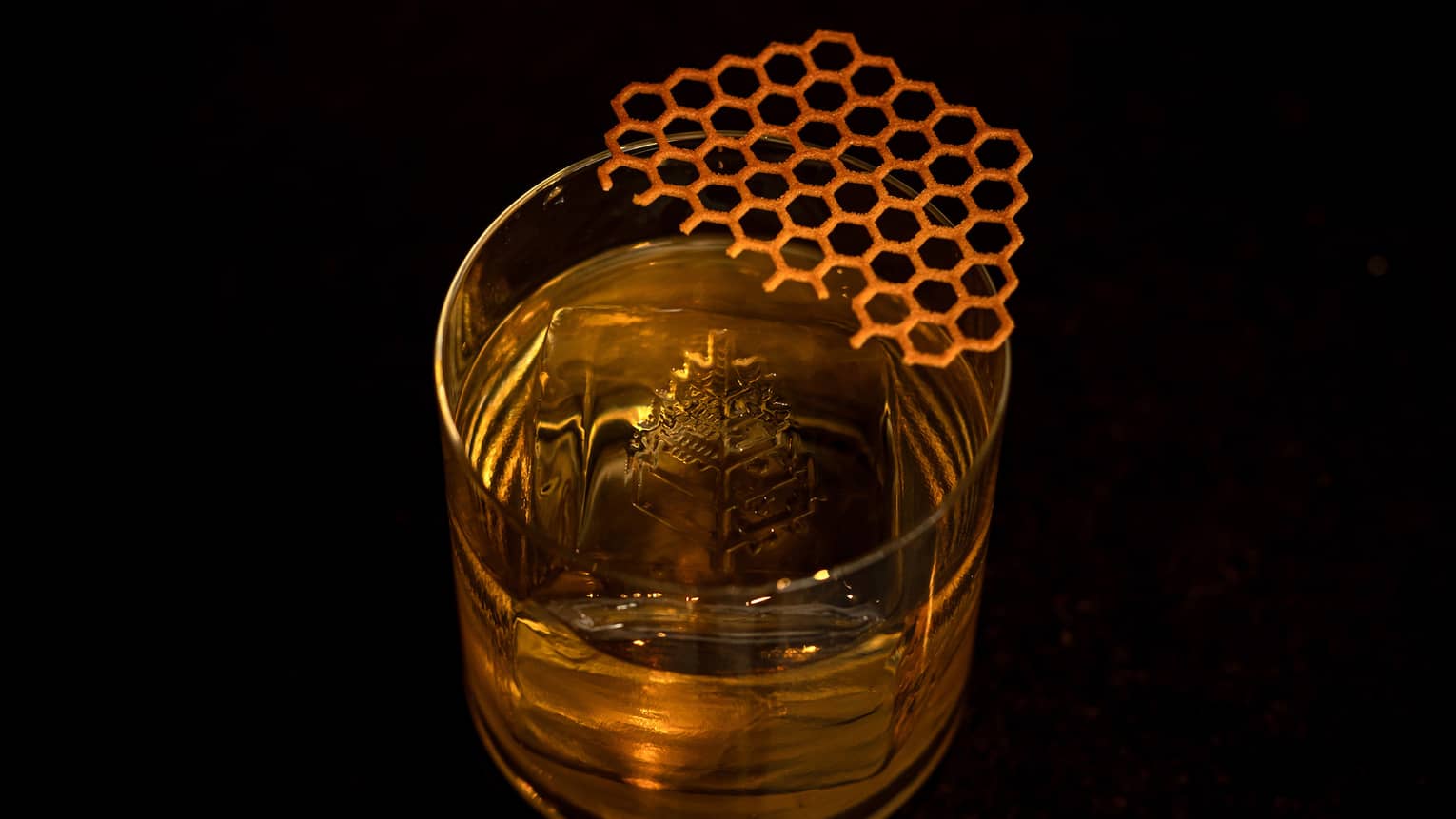 A clear tumbler contains a golden-hued cocktail, ice and garnish
