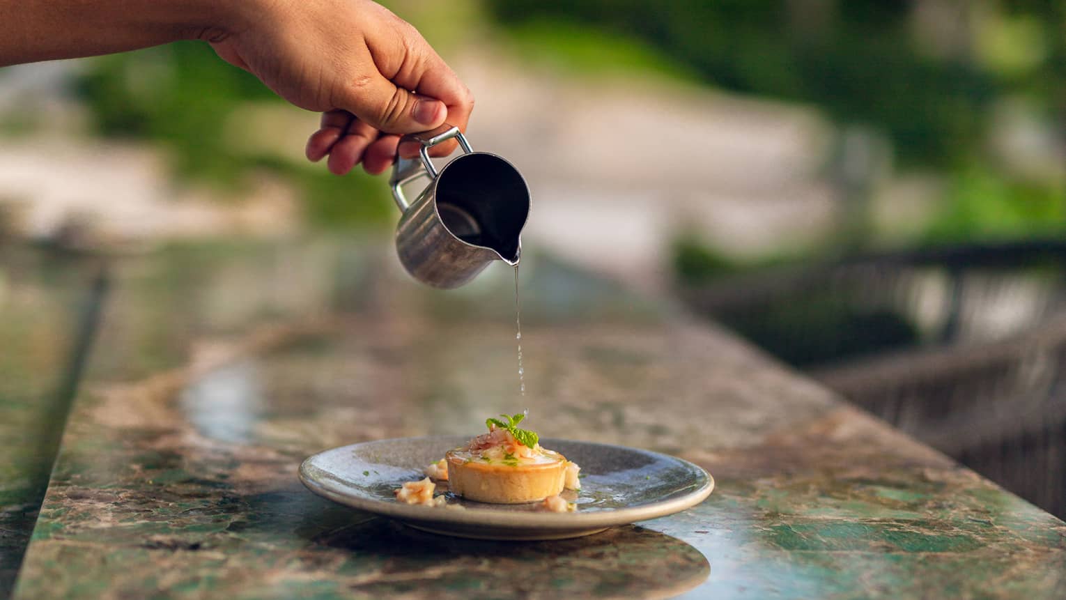 A hand pours sauce over tart dish