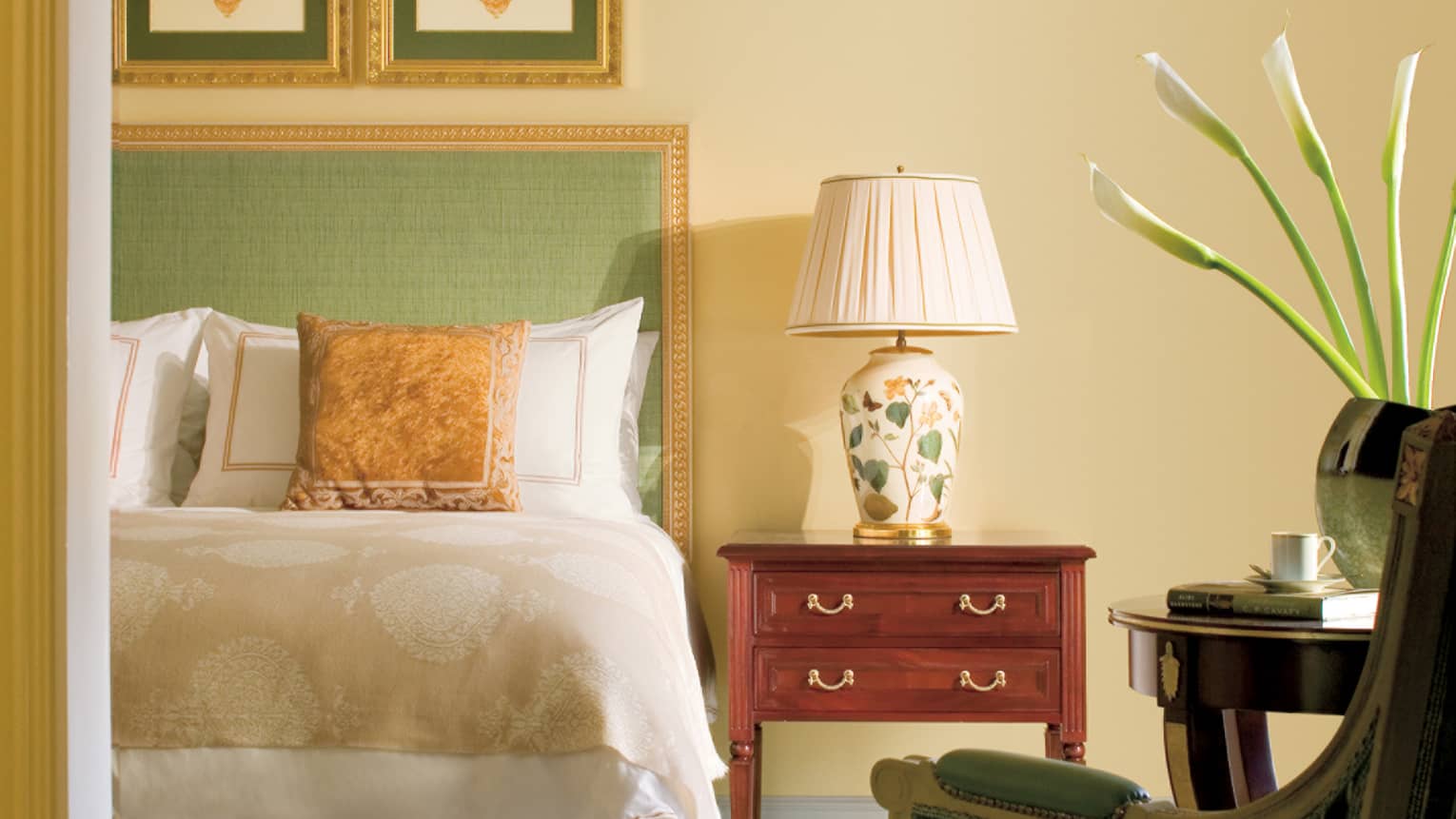Close-up of Deluxe Two-Bedroom Suite bed with green headboard, gold frame and accent pillow, floral bedside lamp