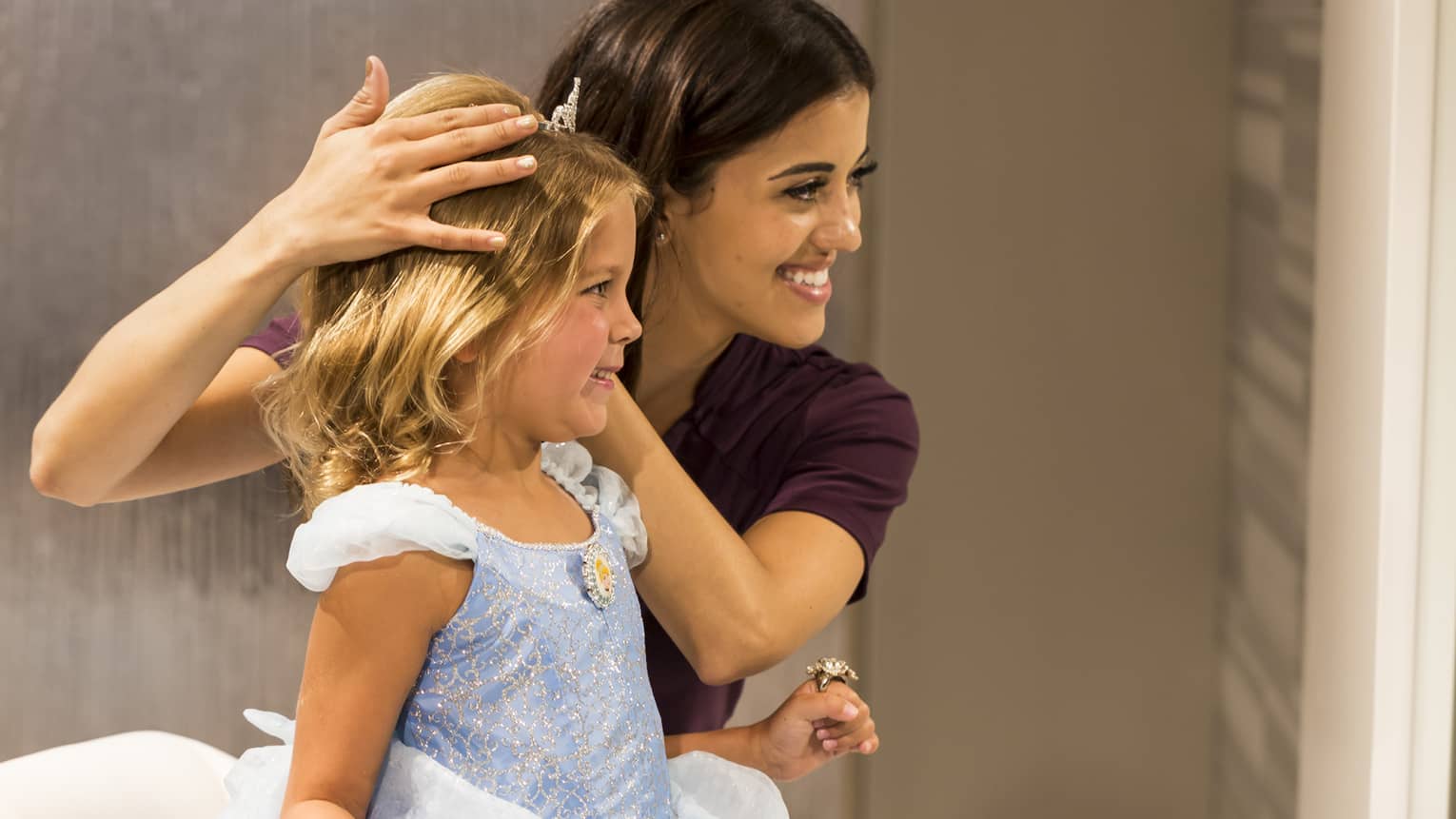 A little girl smiles into a mirror as she is dressed in a Cinderella costume
