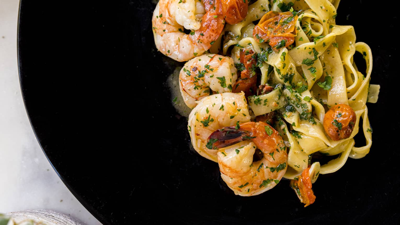 A shrimp pasta on a black plate.