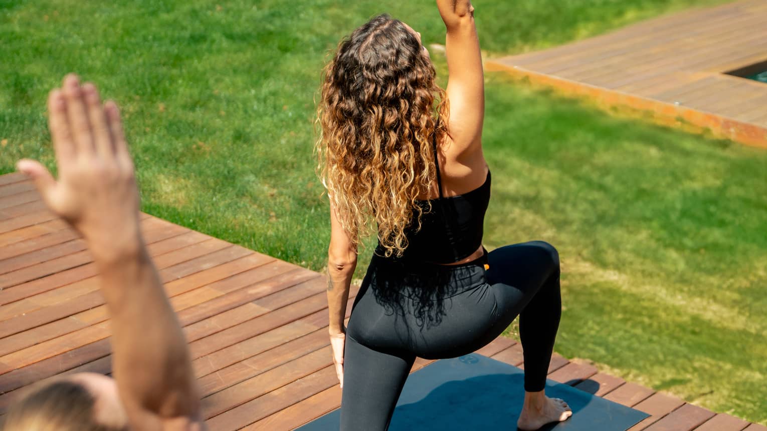 Two people in yoga pose practise on outdoor wooden deck overlooking lush green grass