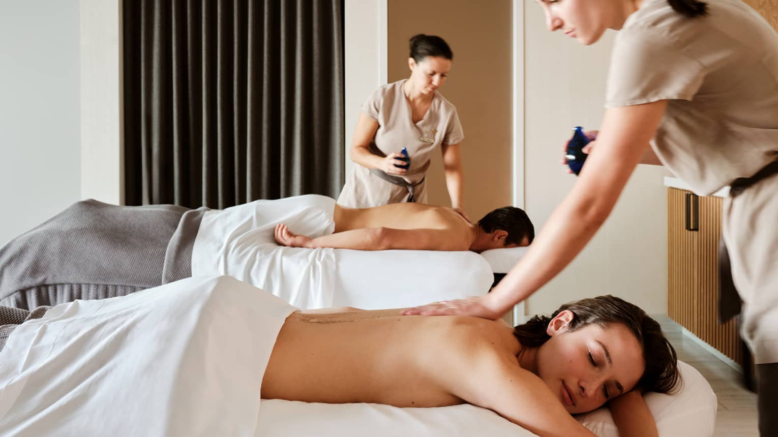 Couple lying prone on spa tables while being massage by spa therapists