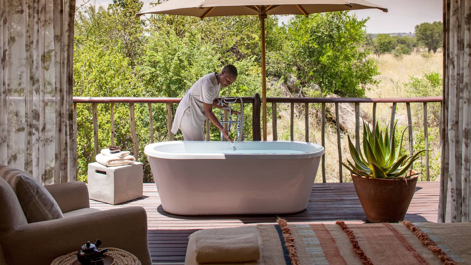 Woman draws bath in freestanding tub on patio beside large cactus plant in pot