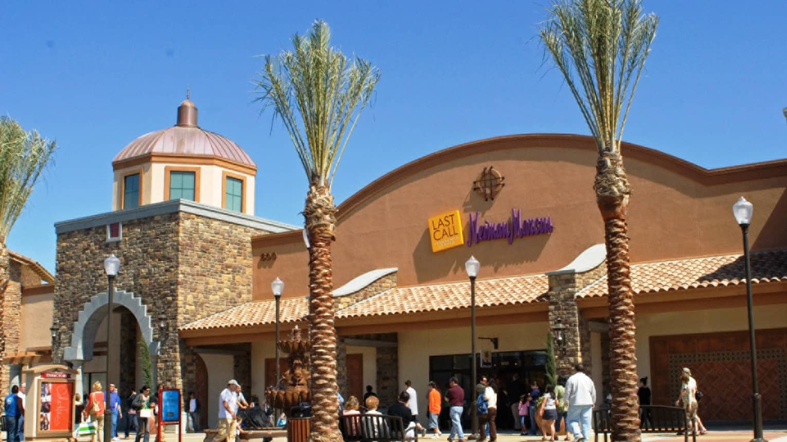 People wandering outside Westlake Village shopping mall with palm trees, blue sky 