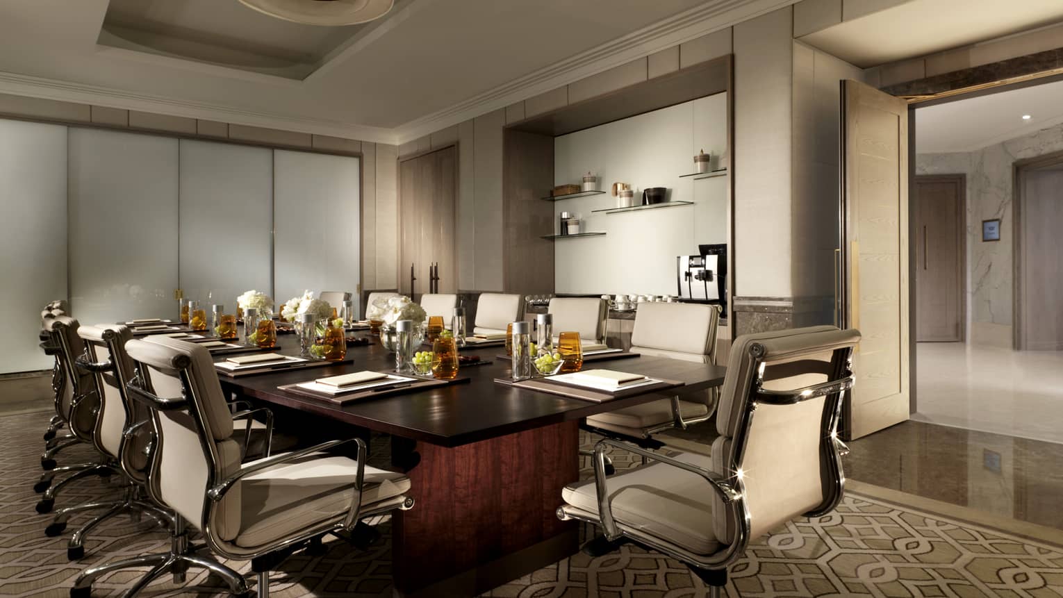 Meeting room with white leather executive swivel chairs around large wood boardroom table with amber glassware 