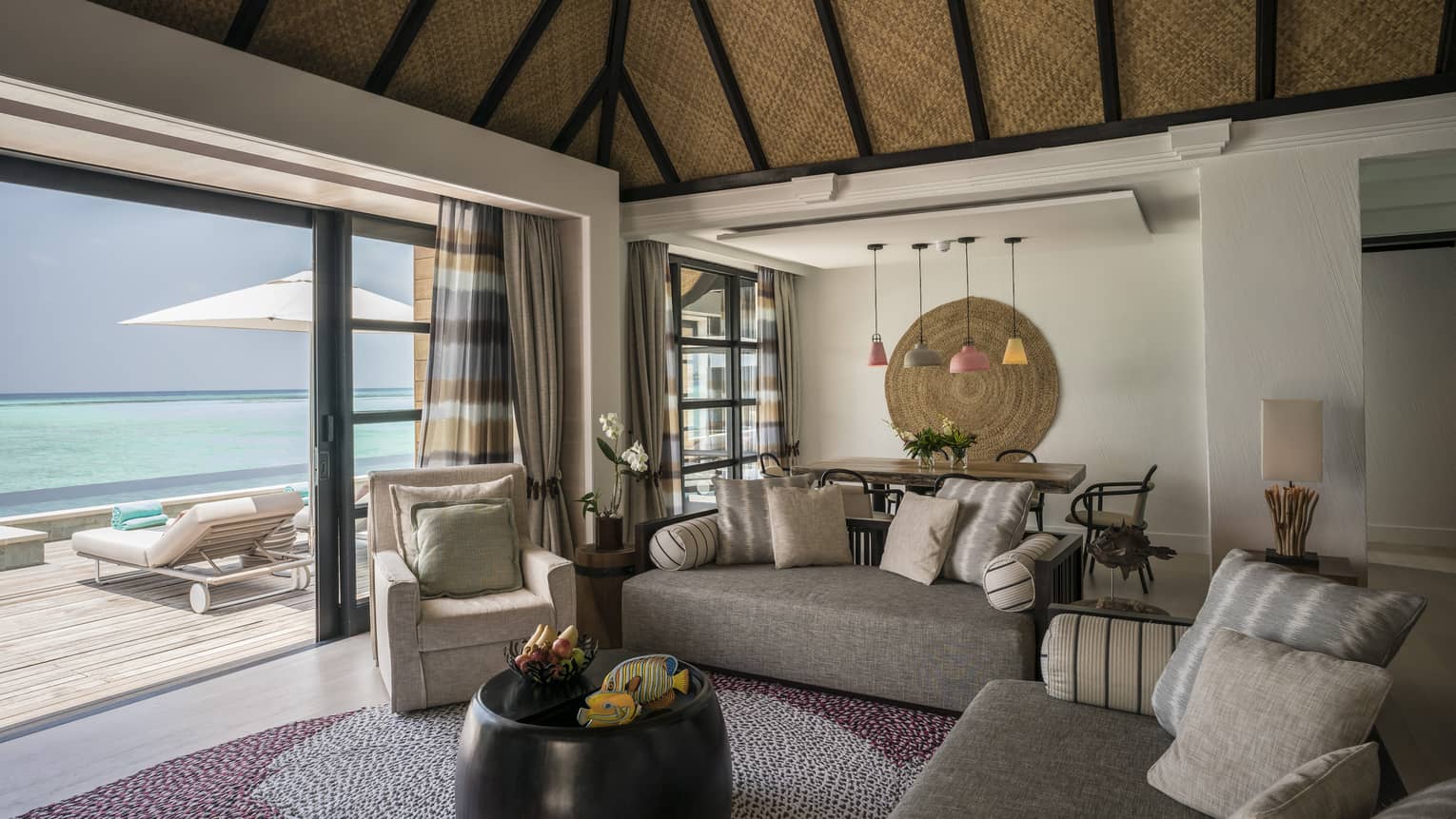 Cozy living and dining area of a water suite, opening to a deck with ocean views 