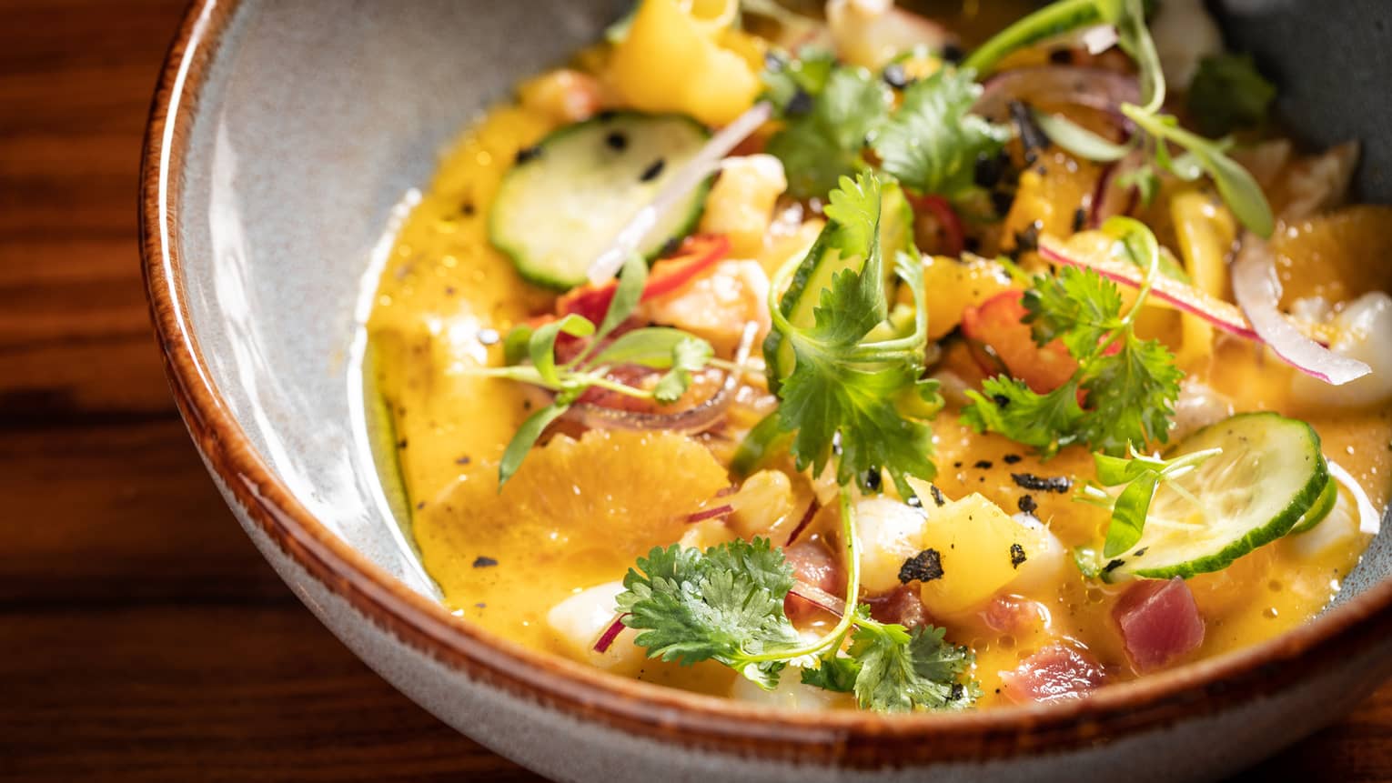 A bowl of yellow ceviche with scallops and shrimp garnished with citrus and cilantro.