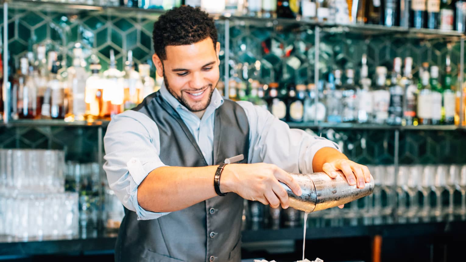 A bartender pouring drinks into multiple glasses on a bar table
