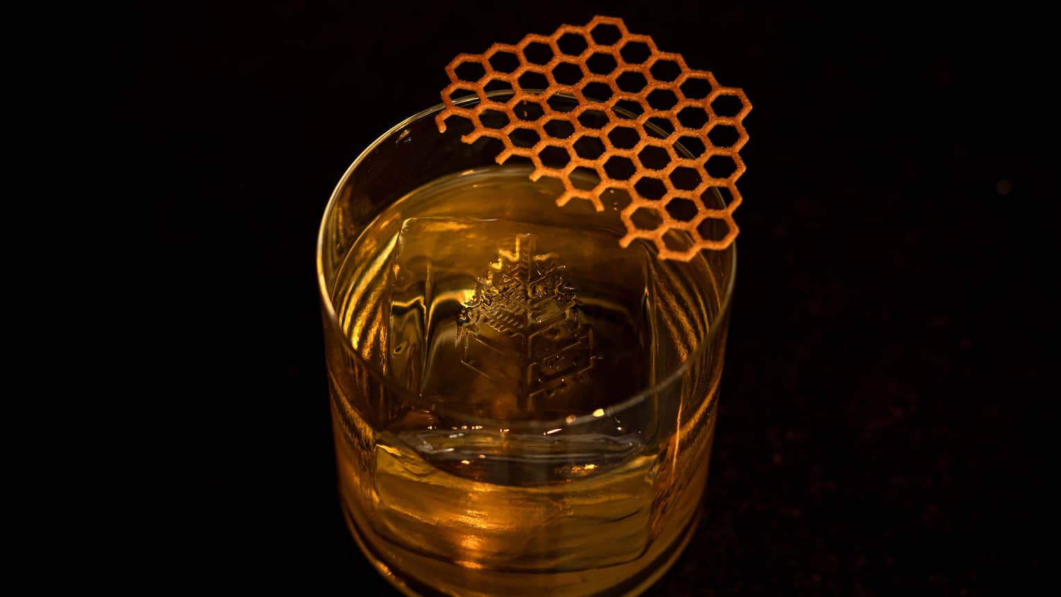A clear tumbler contains a golden-hued cocktail, ice and garnish