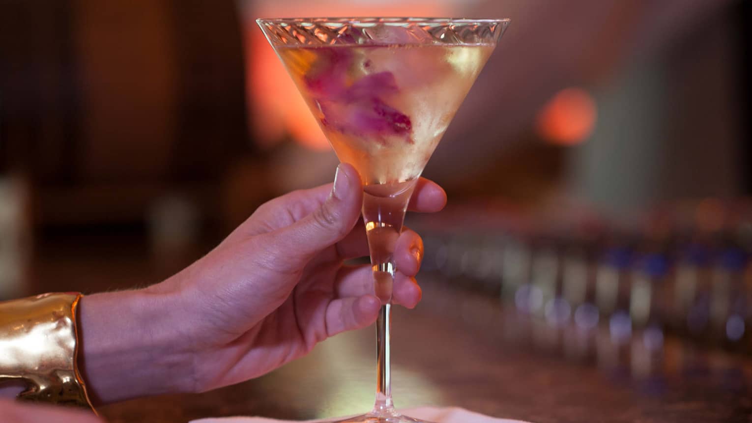 Close-up of hand of woman wearing gold cuff, holding martini glass on bar 