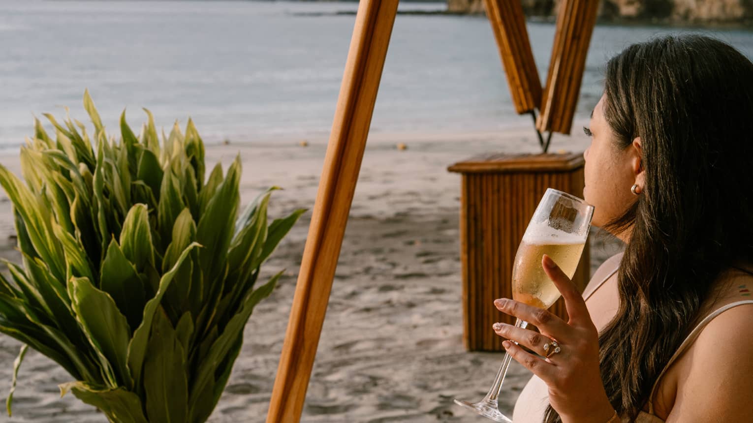 Guest sits on an acapulco chair on the beach while looking out onto the ocean with a beverage in hand