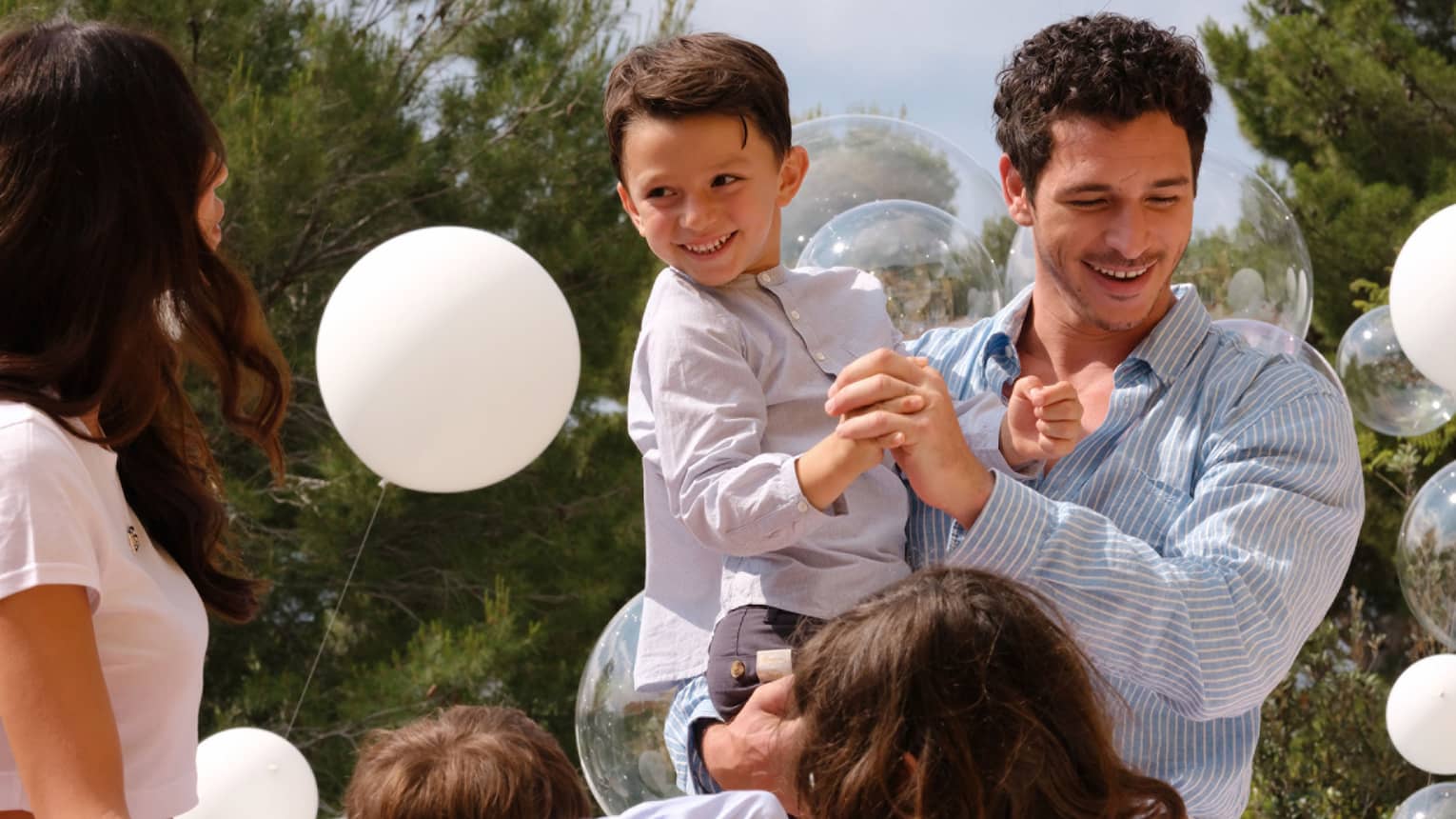 Adult holding a child amid balloons while other adult and kids look on