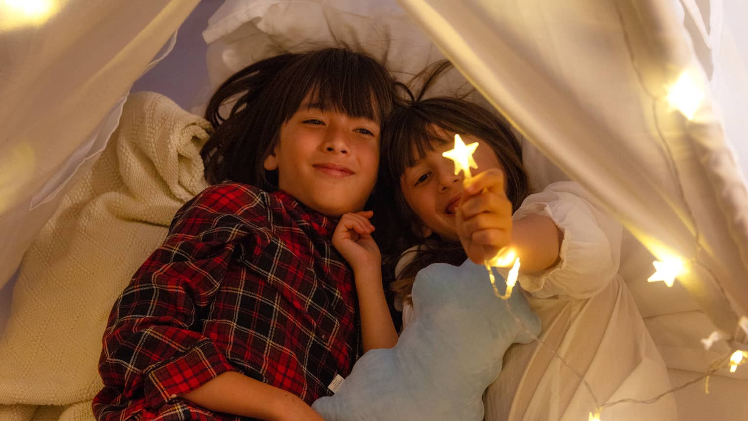 Two kids in an in-room tent with star-shaped string lights.
