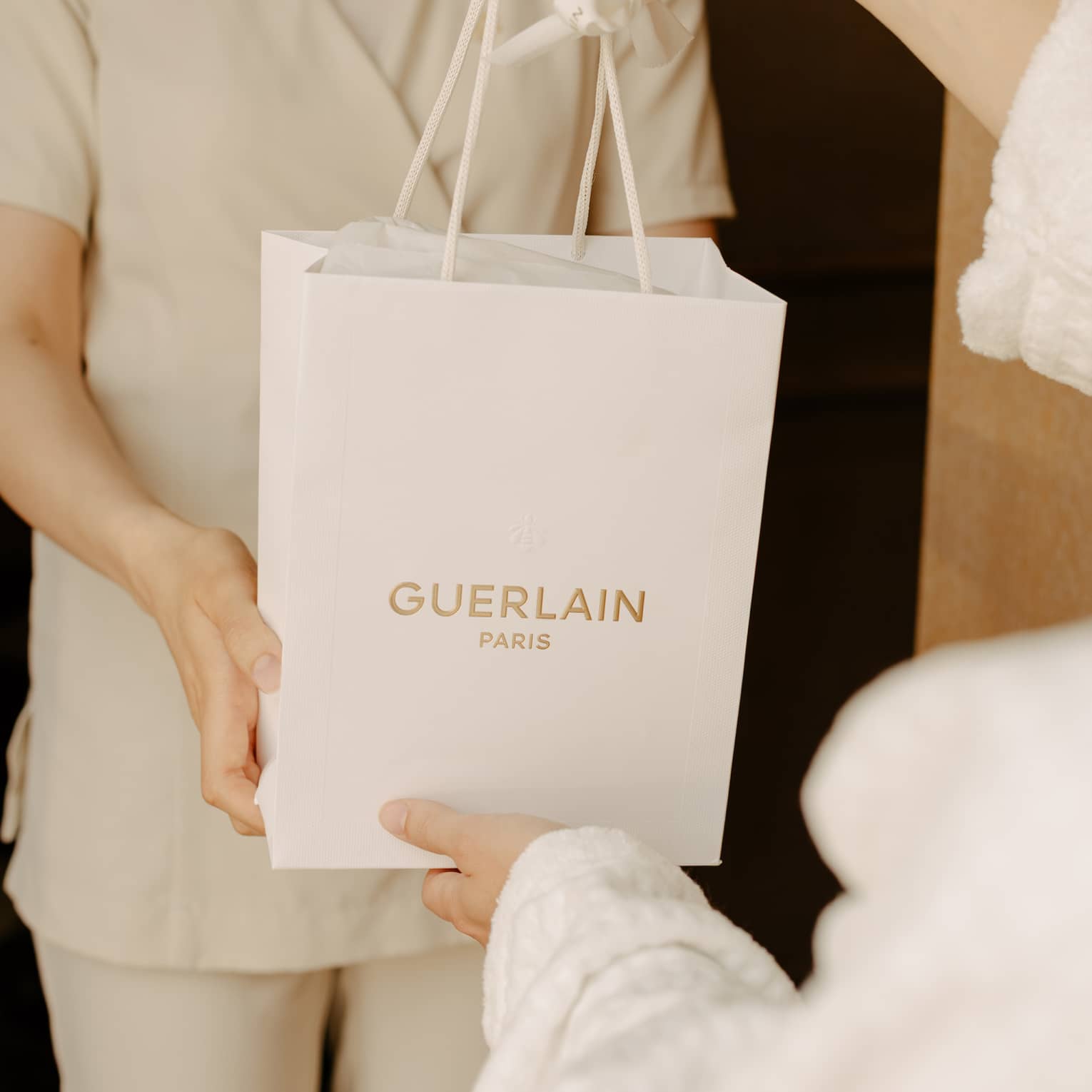 Spa team member wearing ivory scubs hands a guest a white gift bag