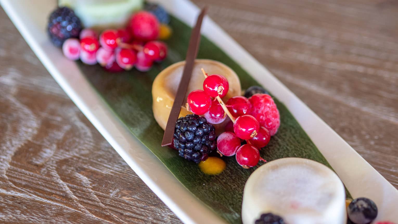 Mochi and berries on a green leaf resting on a white plate.