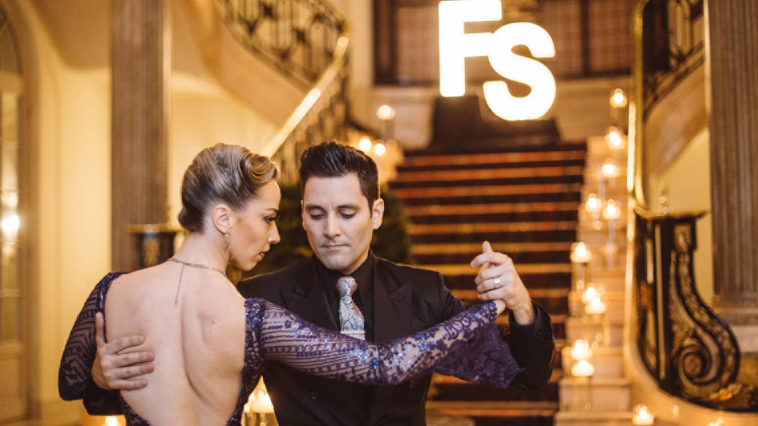 A man and woman tango dancing at the bottom of a wide red carpeting stairway