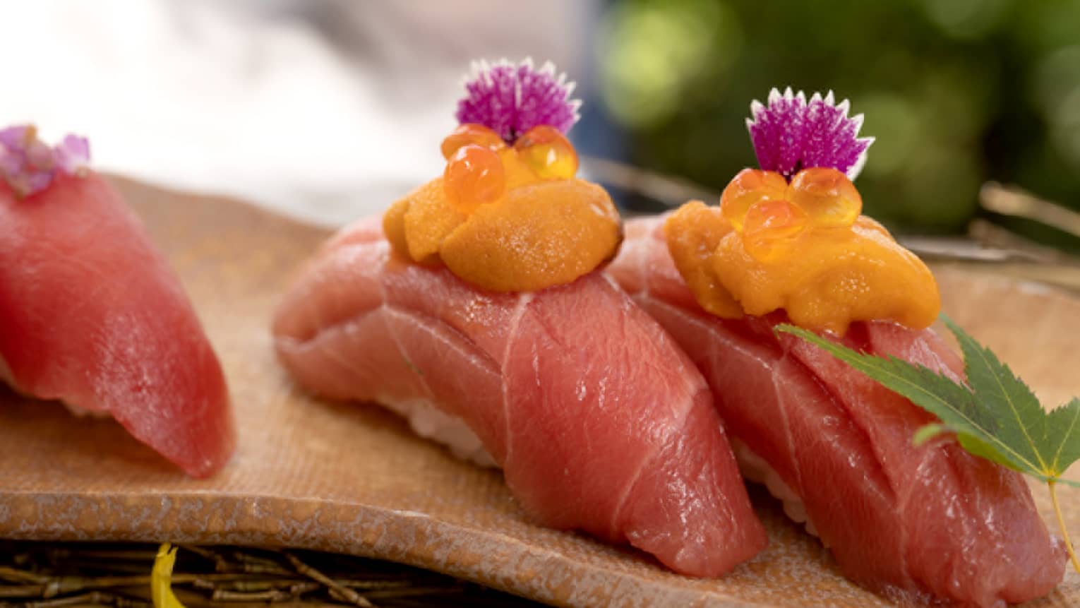Three cuts of sashimi topped with yellow sauce and purple flowers.