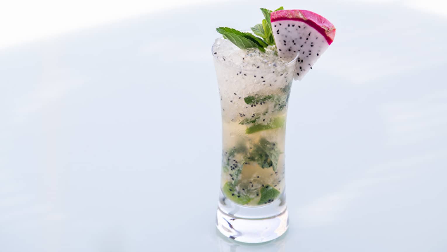 A mojito with a slice of dragonfruit on the side of the glass.