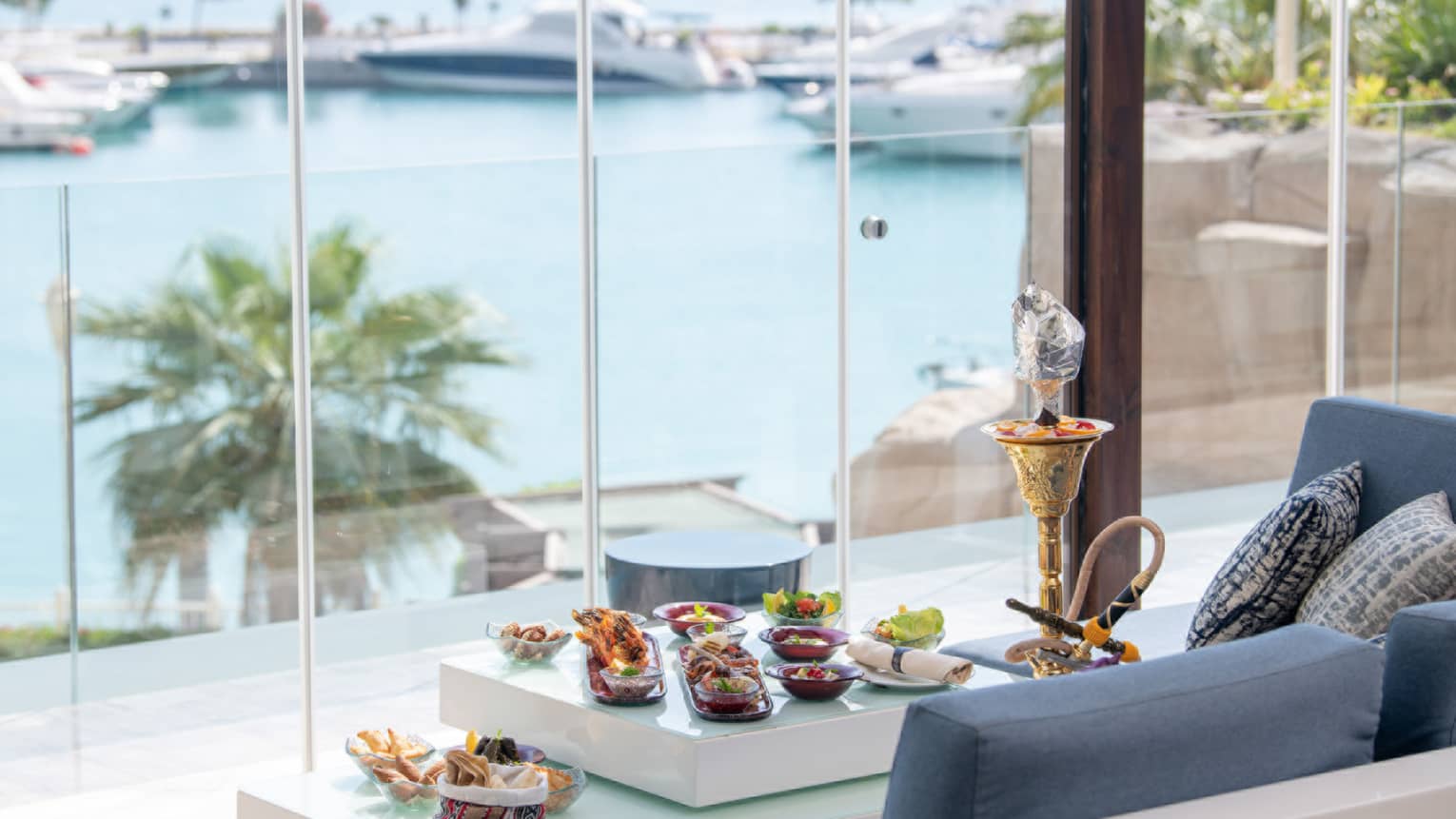 View of the marina through floor-to-ceiling windows at The Terrace, shisha and canap�s on table in front of blue sofa lounge
