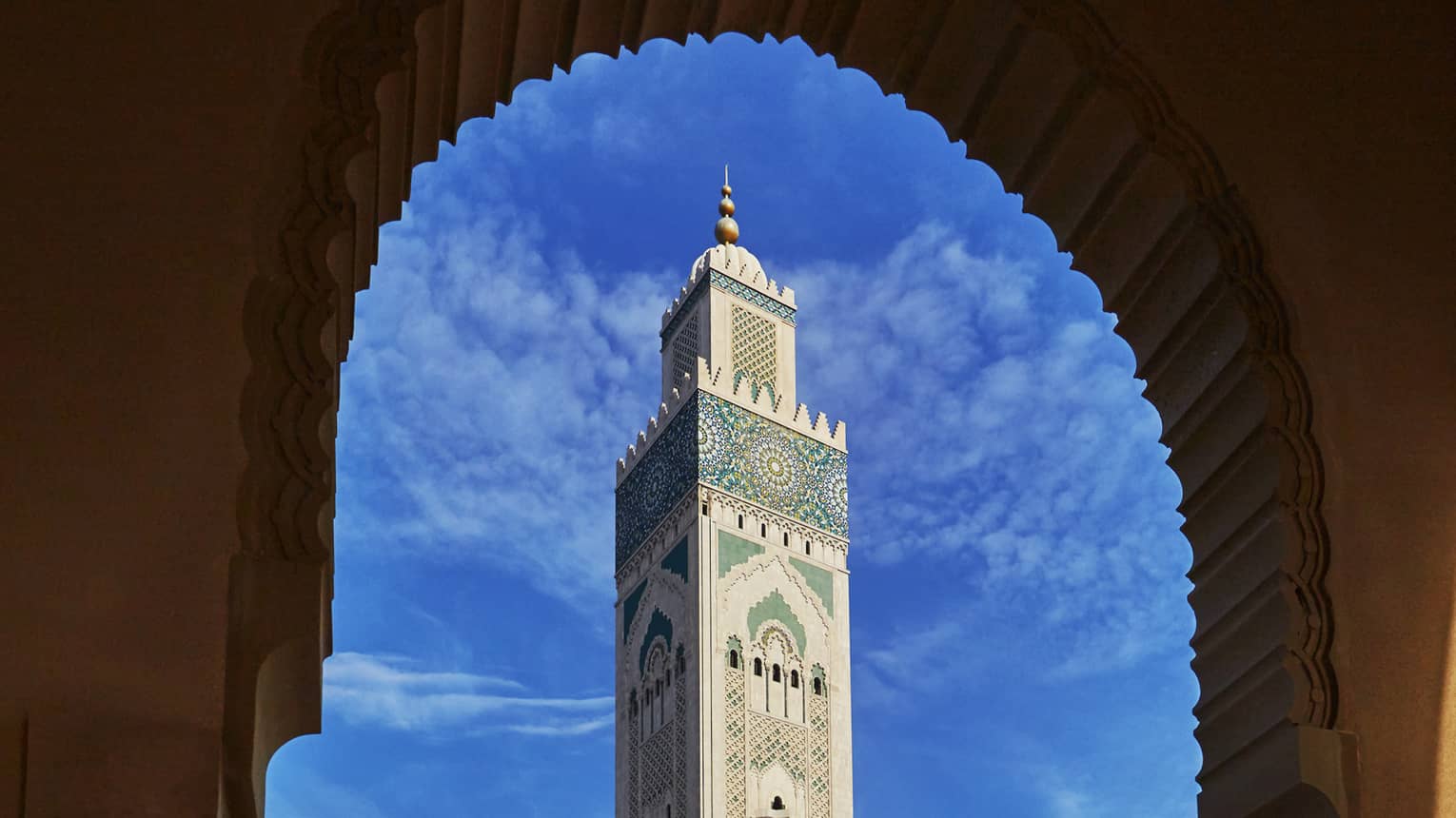 View from archway of Hassan II Mosque tall tower against blue sky 