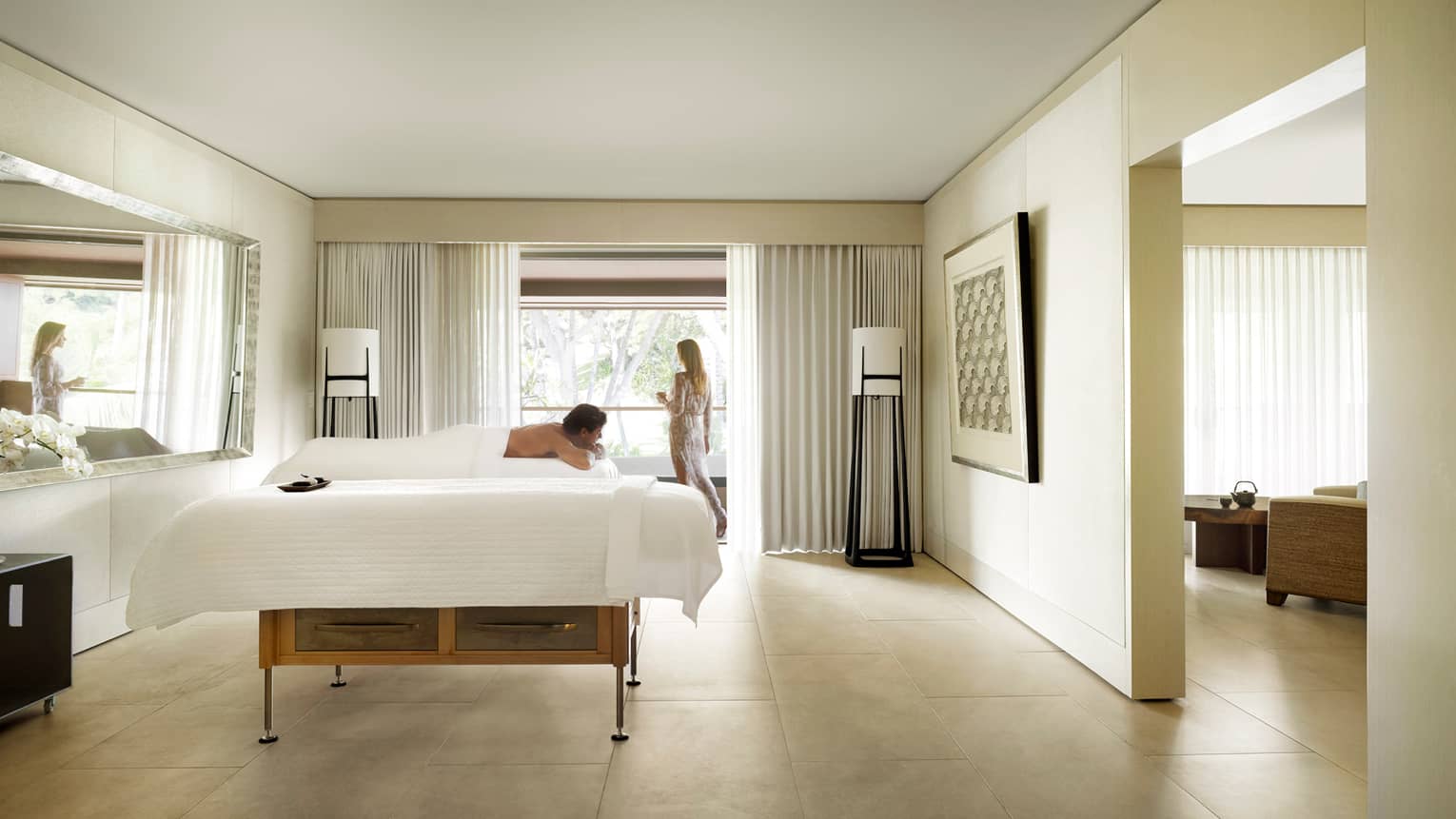 Woman at window, man lies on massage table in Couples Suite in spa