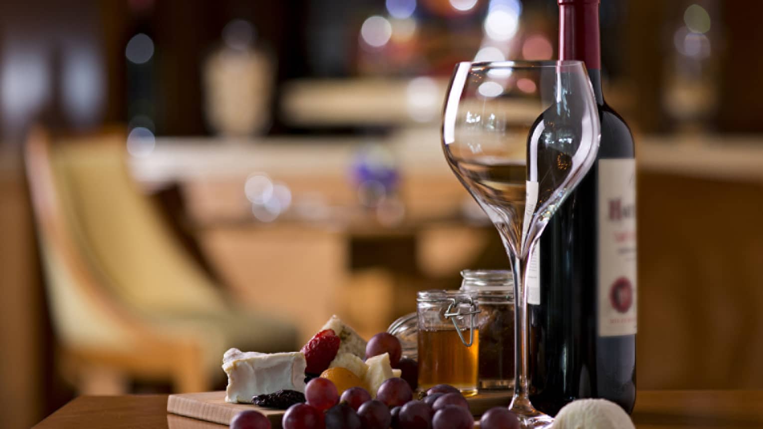 Large empty wine glass next to bottle of red wine, fresh grapes and cheese on counter 