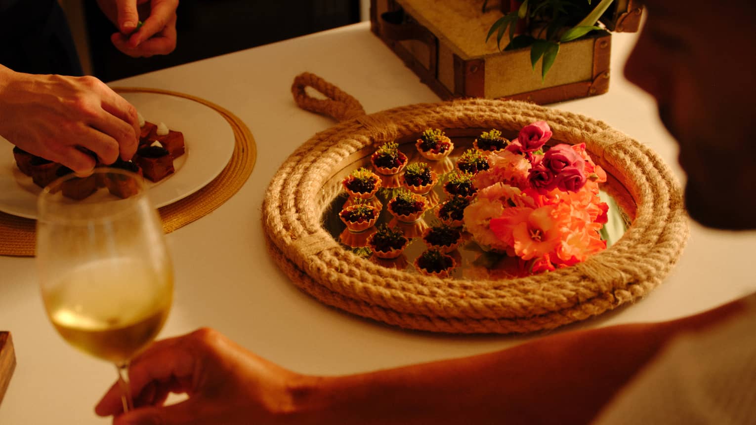 Person sits at a kitchen counter holding a glass of white wine as a chef prepares a plate of appetizers,Person sits at a kitchen counter holding a glass of white wine as a chef prepares a plate of appetizers