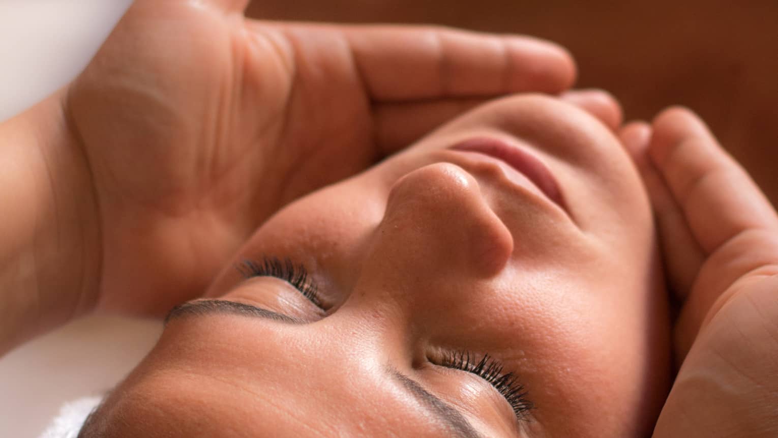 Close-up of woman with eyes closed facing up as hands cup her face and chin