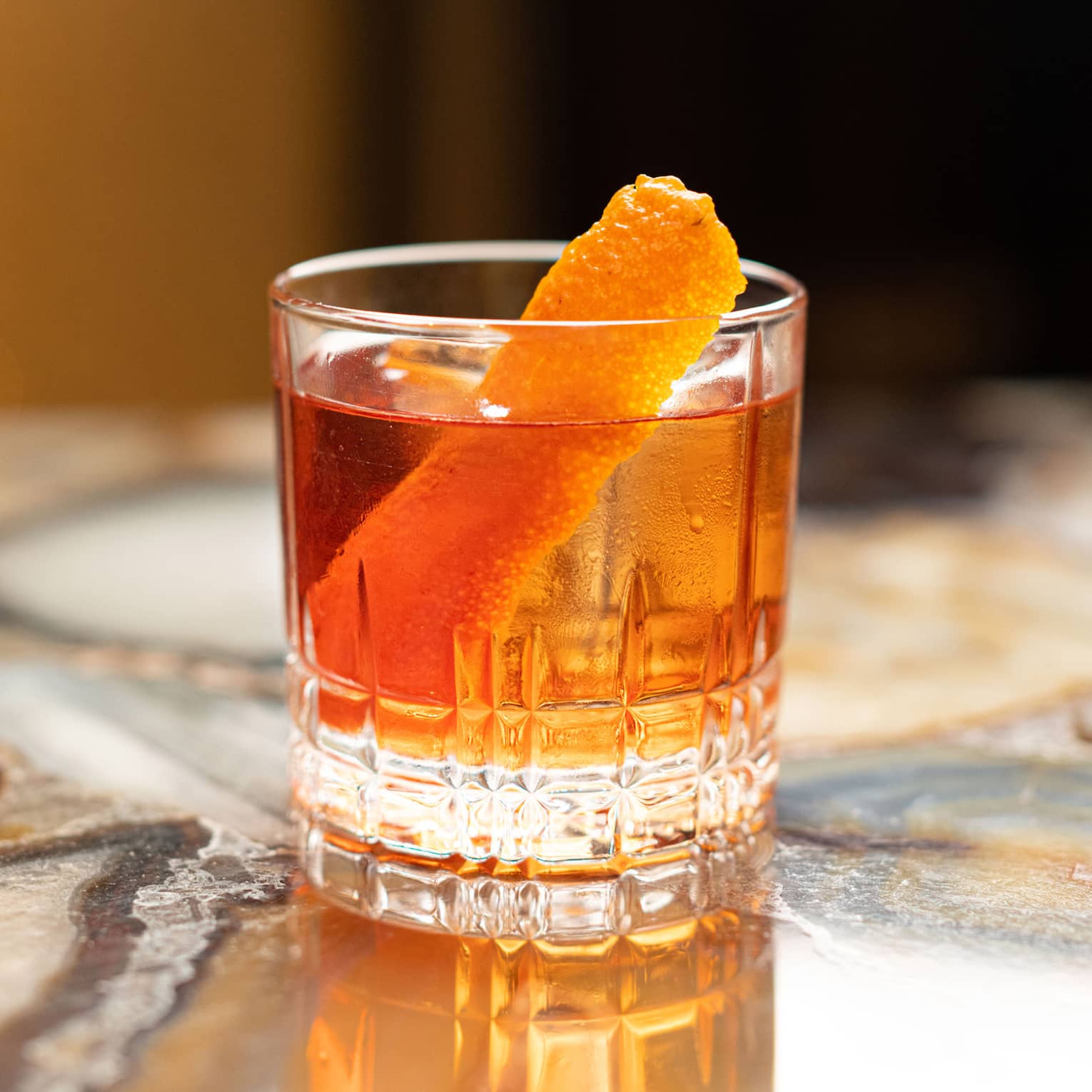 Drinking glass on a table with a large orange slice in it.